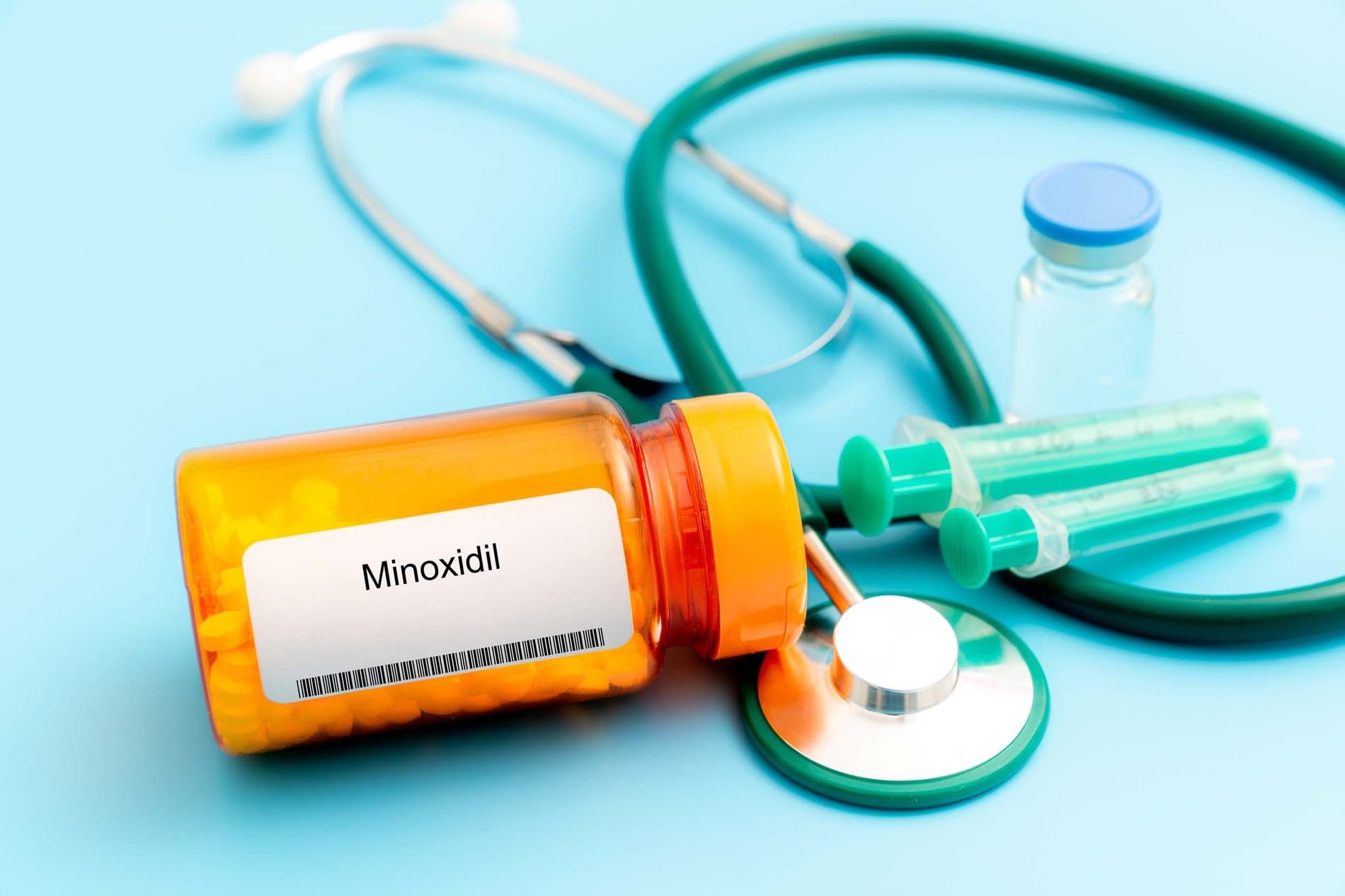 A bottle of Minoxidil tablets beside a stethoscope and syringes, representing medical hair-loss therapy